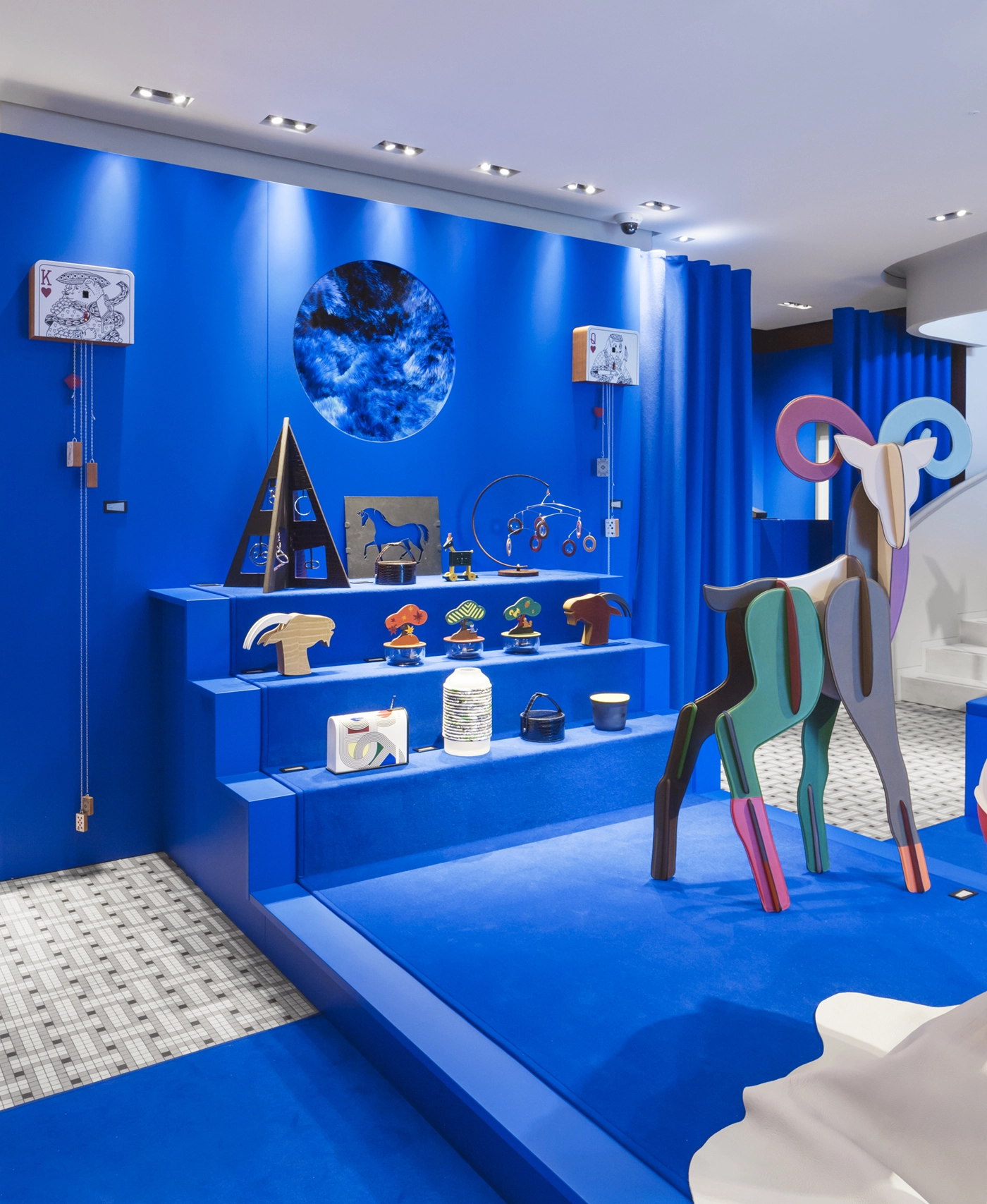 Interior view of Hermès store featuring a blue platform with steps for products and a circular screen