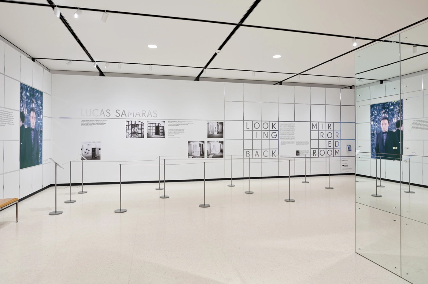 Installation view of Looking Back: Lucas Samaras's Mirrored Room at the Buffalo AKG Art Museum, featuring a grid system in reflective tape as well as wall text and a portrait of the artist